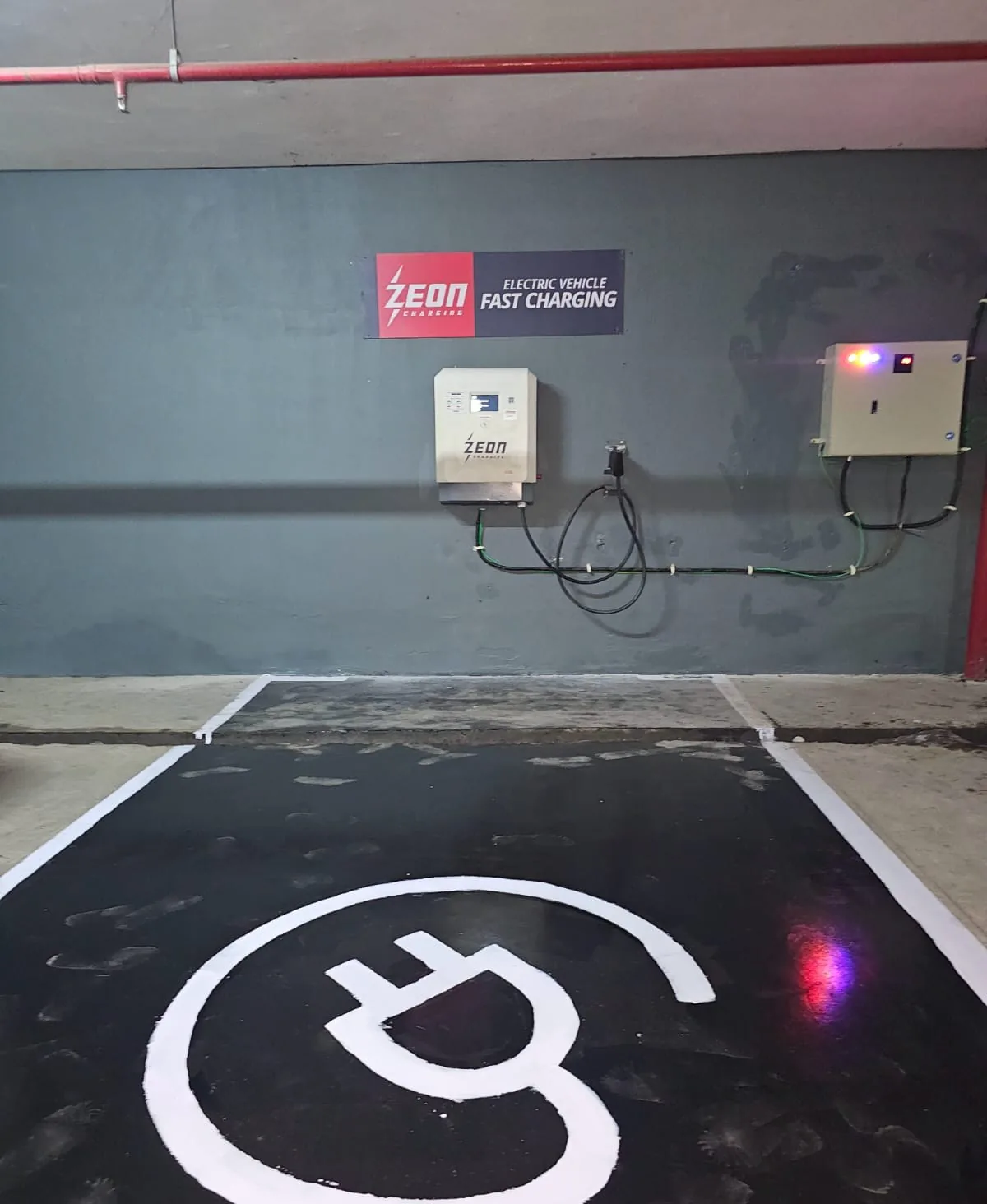 Wall-mounted DC fast charger in a basement with distribution panel and painted EV symbol