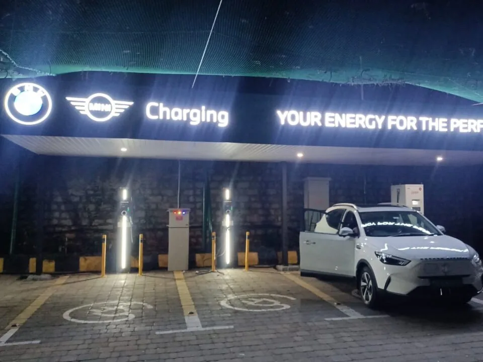 Illuminated BMW MINI charging canopy at night with two AC charge posts, a DC unit and an EV in the marked bay