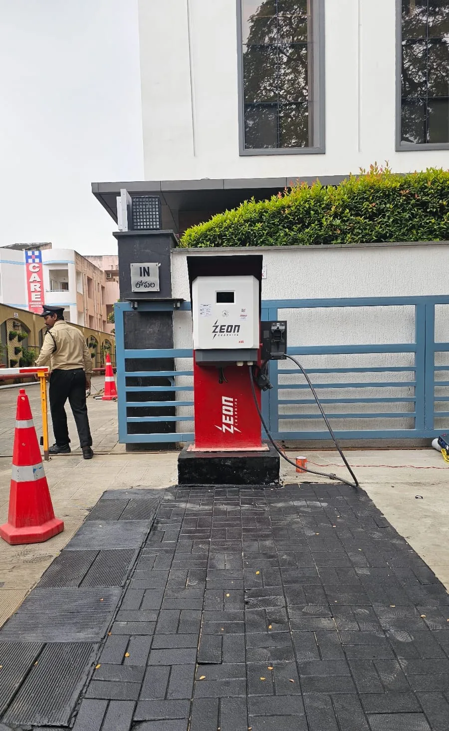 Compact wall-mounted DC charger on a pedestal at a building entrance gate