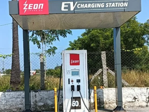 EV charging station canopy with a 60 kW DC charger beside a palm tree on a highway site
