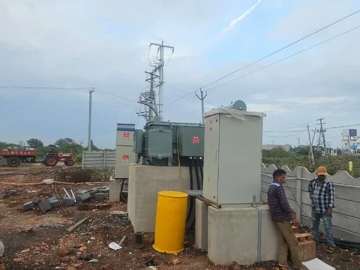 Distribution transformer on a cast plinth beside LT panels and an 11 kV pole structure at a substation under construction